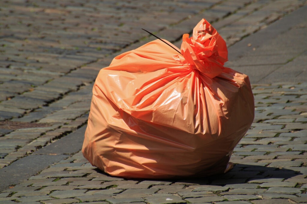 Full orange poop bag on the sidewalk.